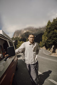 Young man leaning on van during road trip