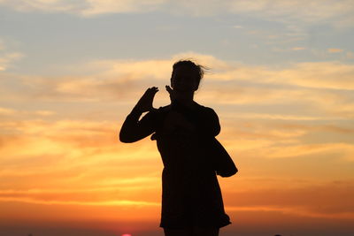 Silhouette of man holding cross against sunset sky