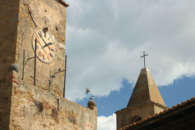 Low angle view of cross amidst buildings against sky