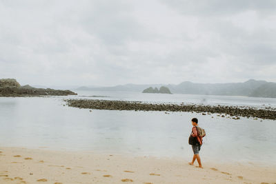 Rear view of man standing on beach against sky