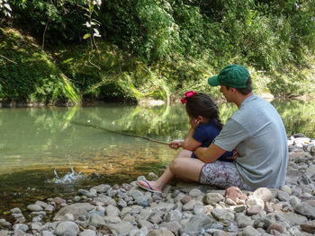 Brother and sister fishing in lake against trees