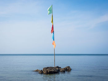 Colorful flag pole on rock in sea against sky