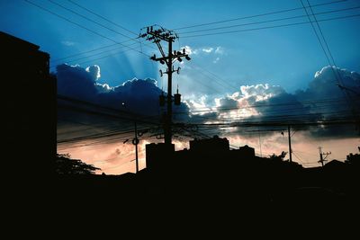 Low angle view of silhouette electricity pylon and buildings against sky