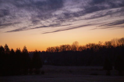 Silhouette trees on field against romantic sky at sunset