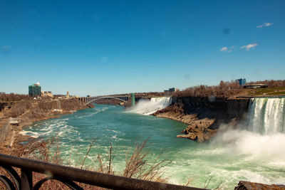 Scenic view of river flowing through city against blue sky