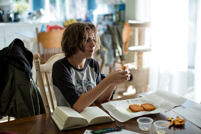 Fourteen year old girl sits at a table with her book and fried snacks