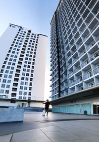Man walking by modern buildings in city against sky