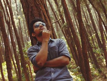Man wearing sunglasses while leaning on trees in forest