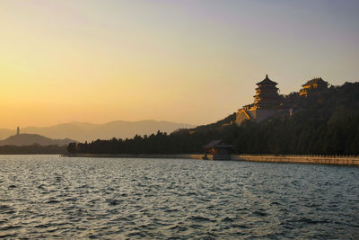 Scenic view of lake by building against sky during sunset