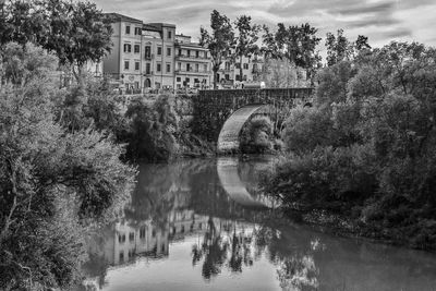 Arch bridge over river by buildings against sky