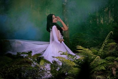 Side view of woman wearing purple evening gown standing by plants in forest