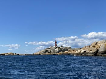 Man standing on rock by sea against blue sky