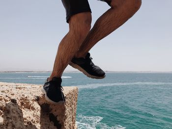Low section of man jumping in sea against clear sky