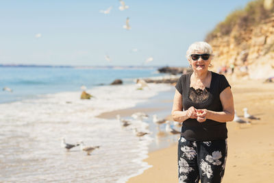 Elderly woman in dark sunglasses feeds seagulls on the beach