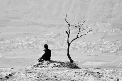 Rear view of woman sitting on beach against sky