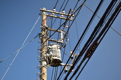 Low angle view of electricity pylon against blue sky