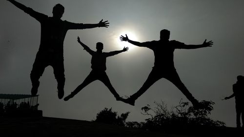 Low angle view of silhouette friends jumping against sky during sunset