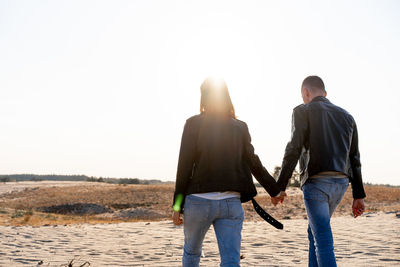 Rear view of couple holding hands walking on field