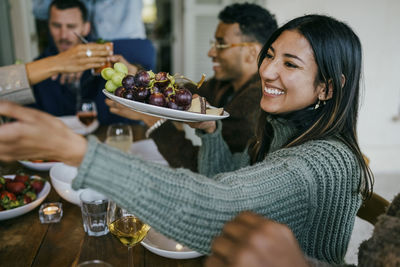 Smiling woman holding fruit plate in patio during dinner party