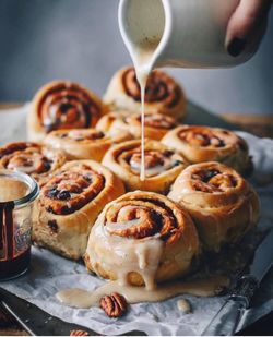 Cropped hand pouring syrup on cinnamon rolls 