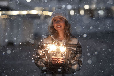 Portrait of smiling young woman holding illuminated christmas tree