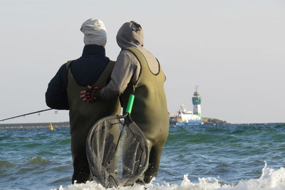 Rear view of men standing in sea against clear sky