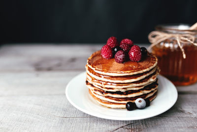 Juicy pancakes with berries and honey on a white plate, spoon, jar, wooden table. high quality photo