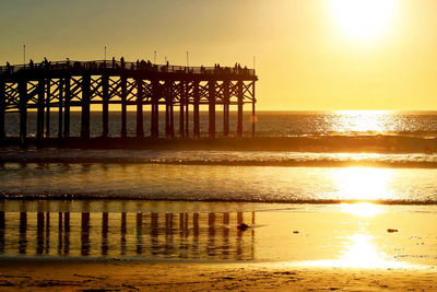 Silhouette of pier on beach during sunset