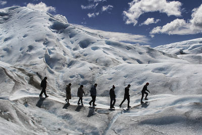 People walking on snowcapped mountain against sky