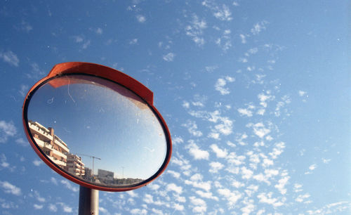 Low angle view of road mirror against sky