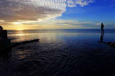 Man standing at beach against sky during sunset