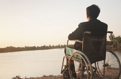 Rear view of man sitting on land against sky