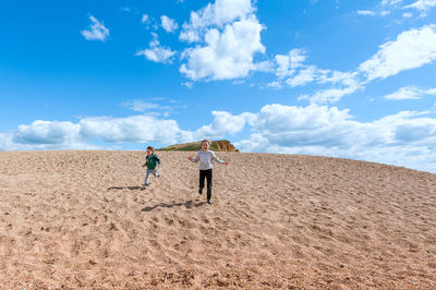 Rear view of people walking on beach against sky