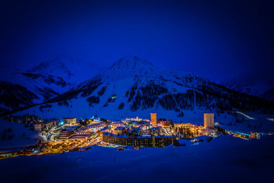 Illuminated houses by snowcapped mountains against sky at night