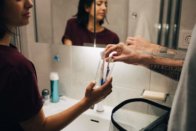 Man and woman keeping toothbrushes in container at illuminated sink