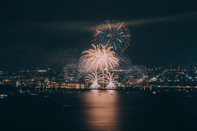 Firework display over illuminated city against sky at night