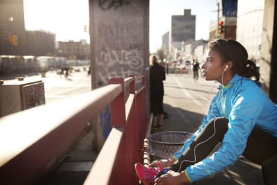 Woman looking away while tying shoe lace in city