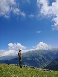 Side view of man wearing sun hat while standing on field against sky