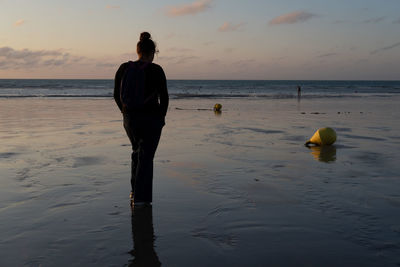 Rear view of man on beach against sky during sunset