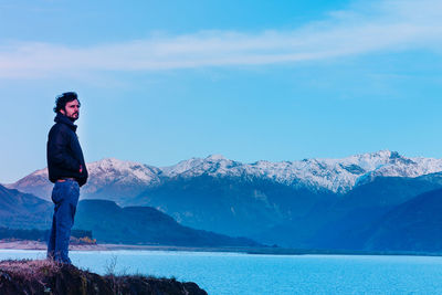 Side view of man standing against snowcapped mountains by lake