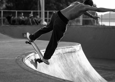 Rear view of teenage boy skateboarder jumping at skatepark