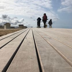 Rear view of people on pier against cloudy sky