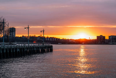 Scenic view of lake by silhouette buildings against sky during sunset