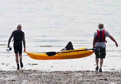 Friends carrying canoe while walking towards sea