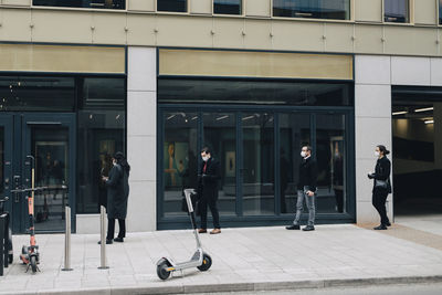 Business people standing in line on footpath by building during covid-19