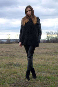 Portrait of young woman standing on field against sky