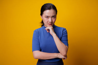 Portrait of young woman standing against yellow background