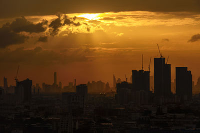 Silhouette of buildings against cloudy sky during sunset