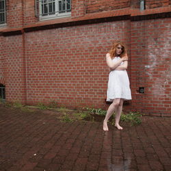 Portrait of young woman embracing herself against building