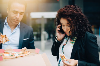 Male and female business colleagues eating pizza against building during lunch